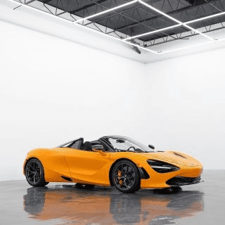 Orange convertible sports car parked in a bright white garage with a glossy floor reflecting the paint
