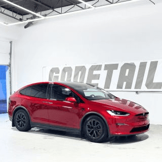 Red electric SUV with black wheels parked inside a bright white garage with a large GoDetail sign on the wall