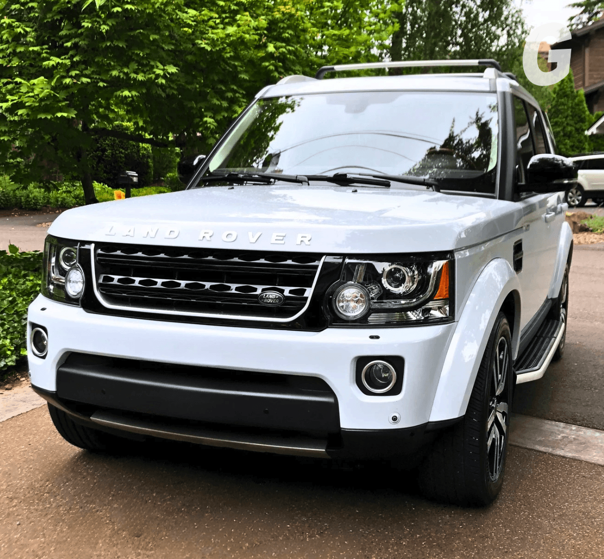 White Land Rover SUV with a glossy finish parked on a driveway in front of green trees and shrubs