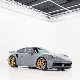 Gray sports coupe with gold wheels parked in a bright white studio with a dark ceiling and strip lights